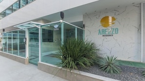A modern building with a glass entrance, a sign for 'AREZZO RESIDENCE', and a marble wall. - Apt in Condo With Easy Access to the sea Are1502 (Guarapari)