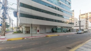 A modern building with a glass facade, a visible storefront with signage, and a clear pedestrian pathway. - Apt in Condo With Easy Access to the sea Are1502 (Guarapari)