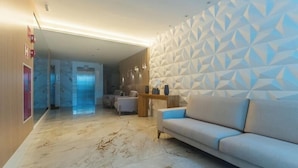 A modern hotel lobby with a marble floor, a sofa, a patterned wall, and an elevator. - Apt in Condo With Easy Access to the sea Are1502 (Guarapari)