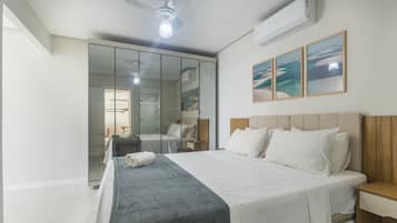 Quarto com cama, mesa de cabeceira, ventilador de teto, ar condicionado, porta de vidro deslizante e parede com três quadros emoldurados.