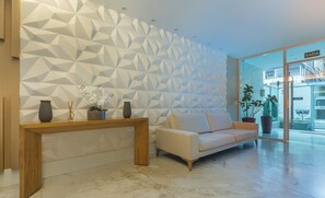 A modern interior with a geometric patterned wall, a wooden console table, a beige sofa, and potted plants. - Apt in Condo With Easy Access to the sea Are1502 (Guarapari)