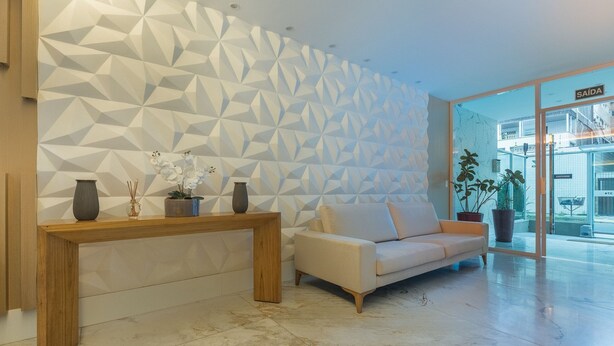 A modern interior with a geometric patterned wall, a wooden console table, a beige sofa, and potted plants. - Apt in Condo With Easy Access to the sea Are1502 (Guarapari)