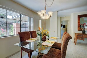 A dining area with a glass table, patterned chairs, a chandelier, and a vase with yellow flowers. - Spacious & modern condo surrounded by resort pools & hot tubs (Palm Springs)