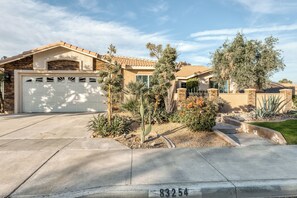 A residential house with a garage, a driveway, and a landscaped garden with various plants and a tree. - Beautiful & spacious home with private pool, spa, and basketball hoop (Indio)
