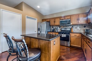 A kitchen with wooden cabinets, stainless steel appliances, and a central island with bar stools. - Beautiful & spacious home with private pool, spa, and basketball hoop (Indio)