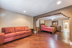 A spacious bedroom with a wooden floor, a red sofa, a bed with a wooden headboard, a dresser, and a mirror on the wall. - Beautiful & spacious home with private pool, spa, and basketball hoop (Indio)