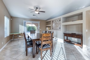 A dining area with a table, chairs, a ceiling fan, and a window with blinds. - Beautiful & spacious home with private pool, spa, and basketball hoop (Indio)