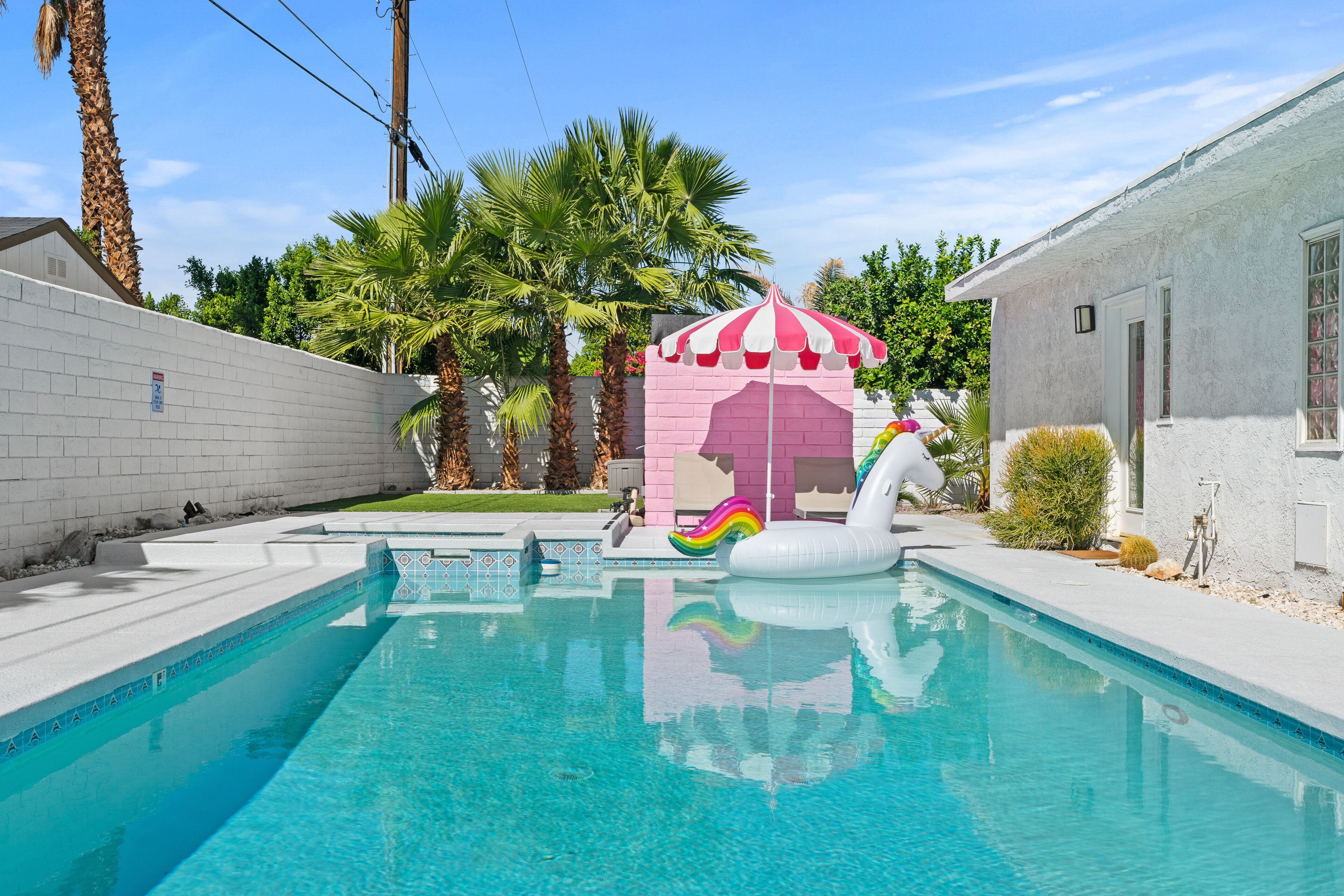 Una piscina con una carpa rosa y blanca, un flotador con forma de cisne blanco y palmeras.