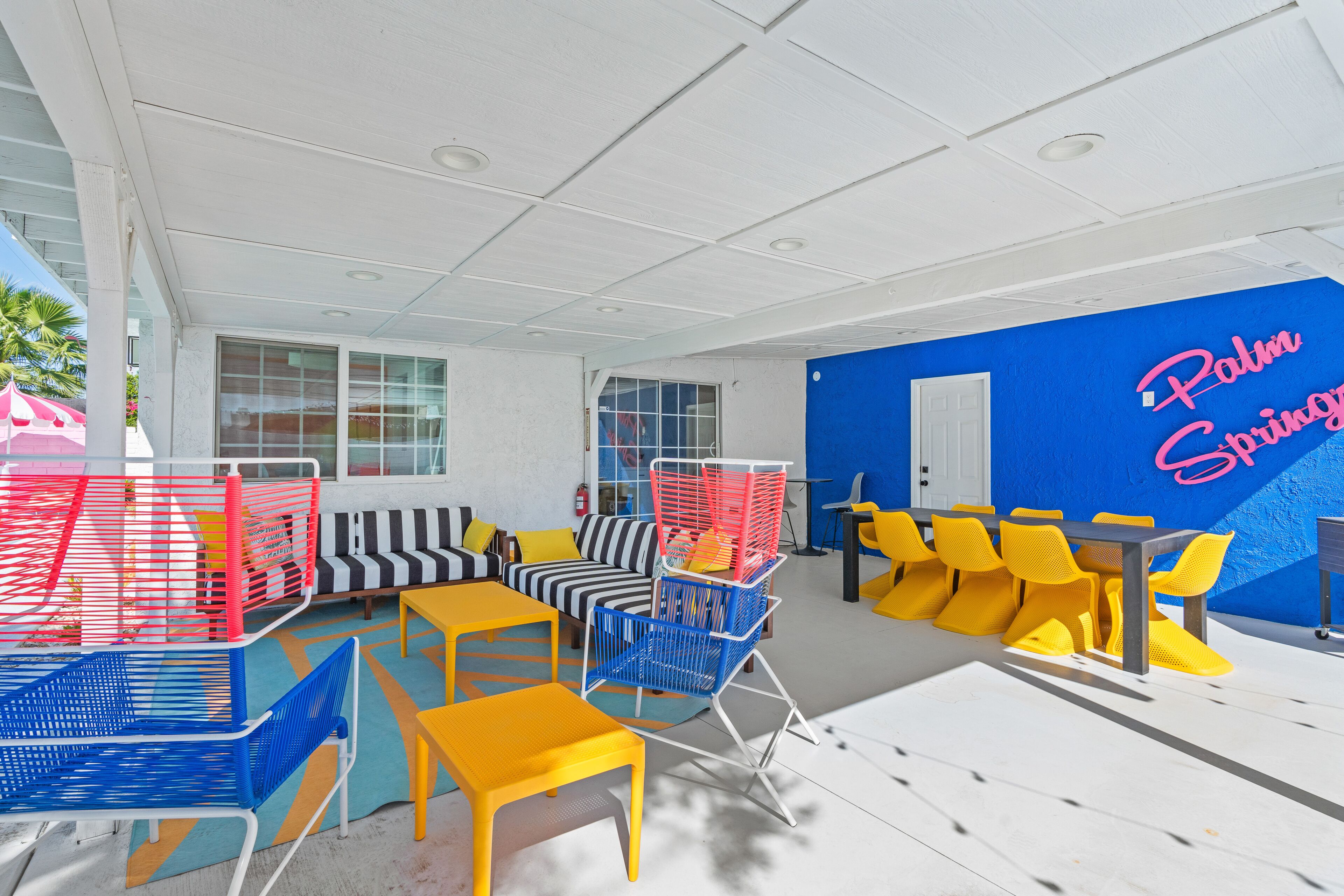 Un espace de détente extérieur moderne, aménagé avec des sièges, notamment des chaises et des canapés, et un mur bleu orné d'une enseigne au néon.