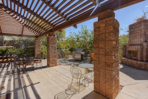 Eine Terrasse im Freien mit einer Pergola, Steinpfeilern, einem Grill und Sitzgelegenheiten.