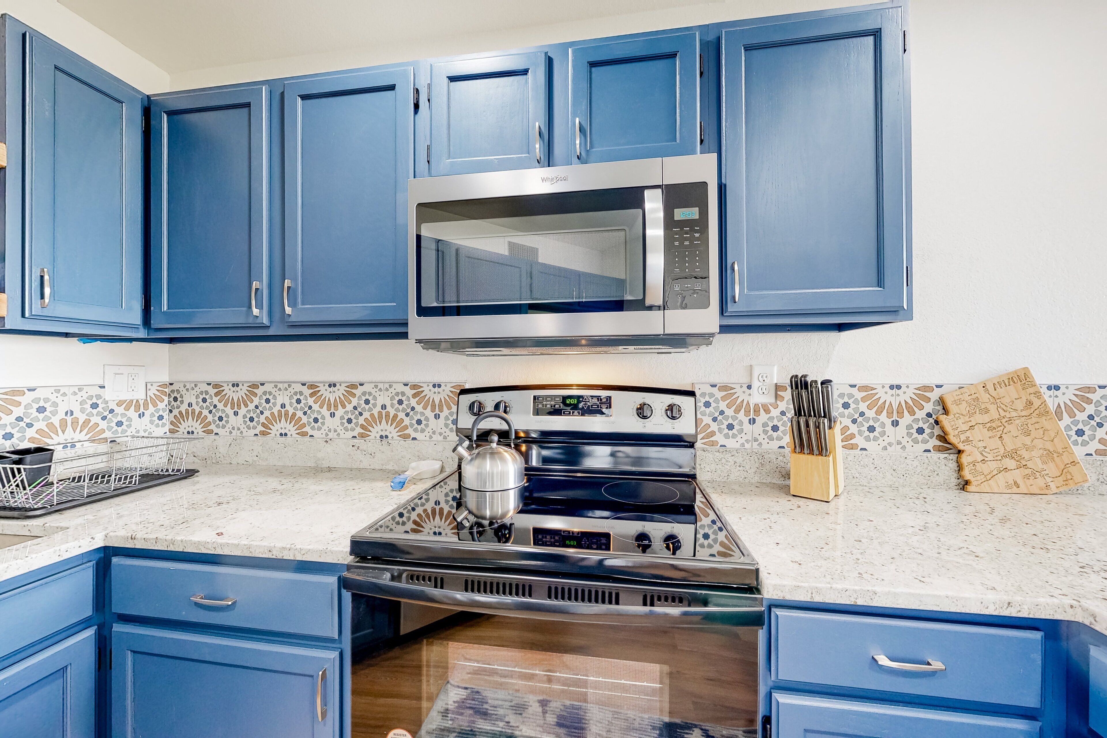 Una cocina con gabinetes azules, microondas, estufa y salpicadero de azulejos.
