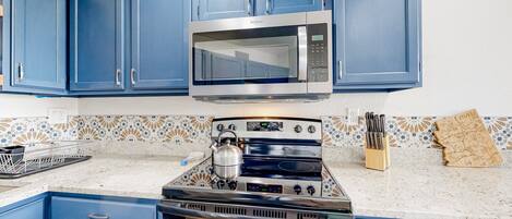 Una cocina con gabinetes azules, microondas, estufa y salpicadero de azulejos.