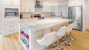 A modern kitchen with white cabinetry, a marble island, stainless steel appliances, and bar stools. - Indulge in Luxury and Comfort in Scottsdale, AZ where cozy meets chic (Scottsdale)