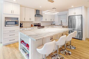 A modern kitchen with white cabinetry, a marble island, stainless steel appliances, and bar stools. - Indulge in Luxury and Comfort in Scottsdale, AZ where cozy meets chic (Scottsdale)