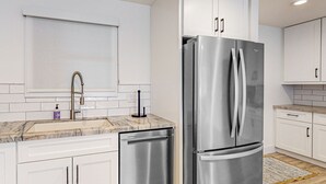 A modern kitchen with white cabinets, a stainless steel refrigerator, a built-in dishwasher, and a marble countertop. - Indulge in Luxury and Comfort in Scottsdale, AZ where cozy meets chic (Scottsdale)