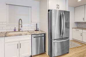A modern kitchen with white cabinets, a stainless steel refrigerator, a built-in dishwasher, and a marble countertop. - Indulge in Luxury and Comfort in Scottsdale, AZ where cozy meets chic (Scottsdale)