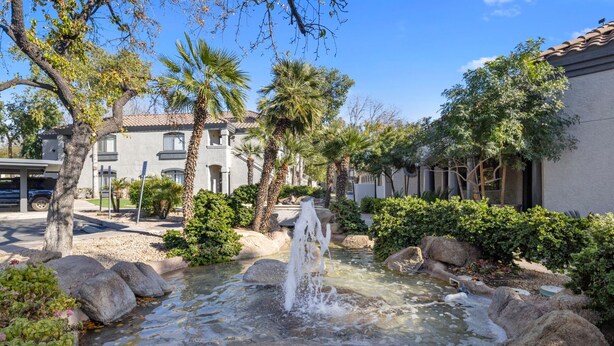 A tranquil outdoor setting with a small water feature surrounded by rocks and greenery, including palm trees and shrubs. - Scottsdale Bliss – Stylish Long Term, Comfort, and Mountain Views Await! (Scottsdale)