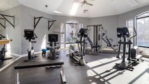 A gym with various exercise machines, a ceiling fan, and large windows allowing natural light. - Scottsdale Bliss – Stylish Long Term, Comfort, and Mountain Views Await! (Scottsdale)