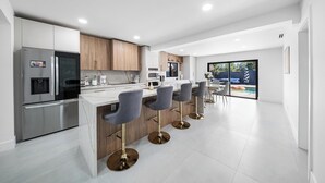 Une cuisine moderne dotée d’un îlot central, de tabourets de bar et offrant une vue sur un jardin avec une piscine.