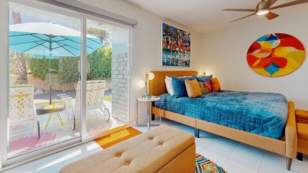Une chambre moderne avec un grand lit, un ventilateur de plafond et une vue sur une terrasse extérieure, accessible par des portes vitrées.