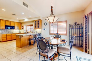 A spacious kitchen with wooden cabinets, a central island, and a dining area with a round table and chairs. - Snowbird-friendly house with mountain view, pool, on-site golf, and central AC (Indio)