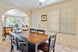 A dining room with a wooden table and chairs, a white door, and a window with blinds. - Beautiful condo near downtown w/ shared pools - golf on-site (Palm Springs)