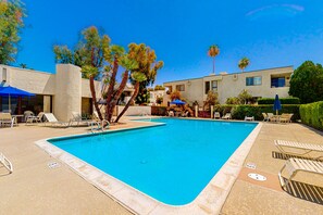 A rectangular swimming pool with a clear blue water, surrounded by lounge chairs and umbrellas, with a building in the background. - Inviting condo w/ gas grill & shared pool/spa/tennis - 1/2 block to El Paseo (Palm Desert)