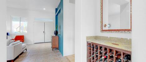 A modern interior with a white sofa, a wooden cabinet, a wine rack, and a tiled backsplash.