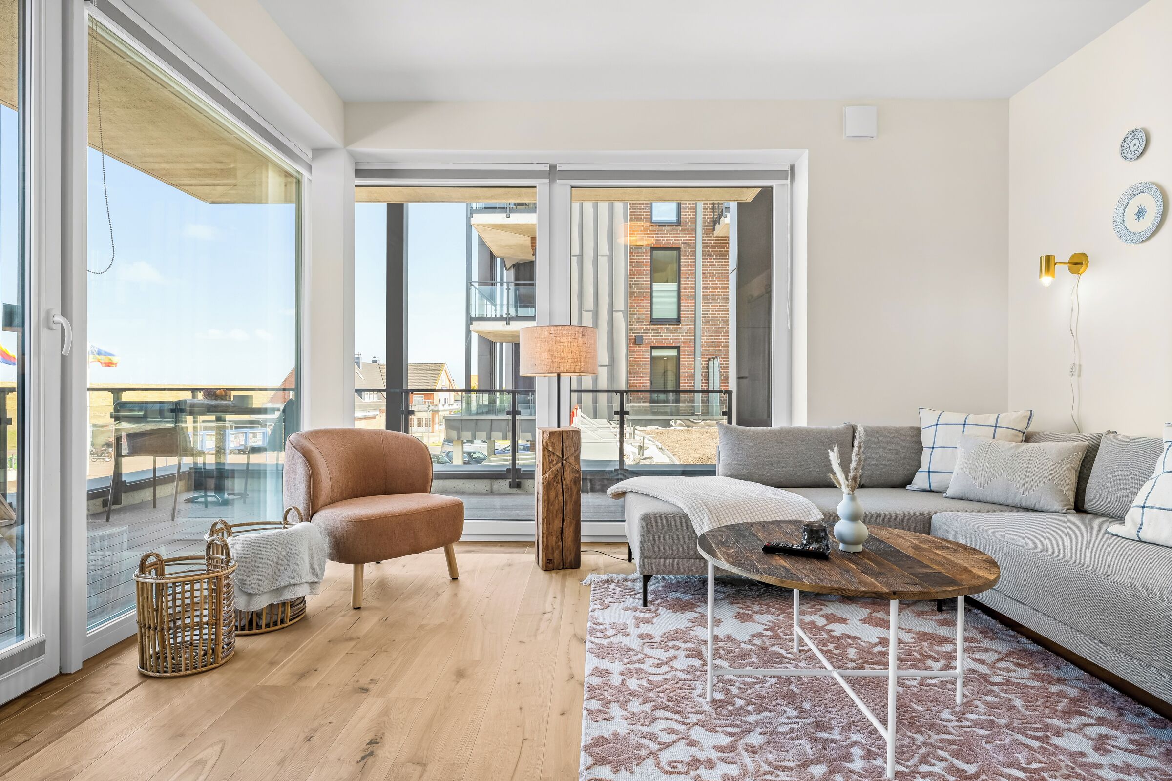 Ein modernes Wohnzimmer mit einer Couch, einem Sessel, einem Couchtisch und Blick auf eine Stadtlandschaft durch große Fenster.