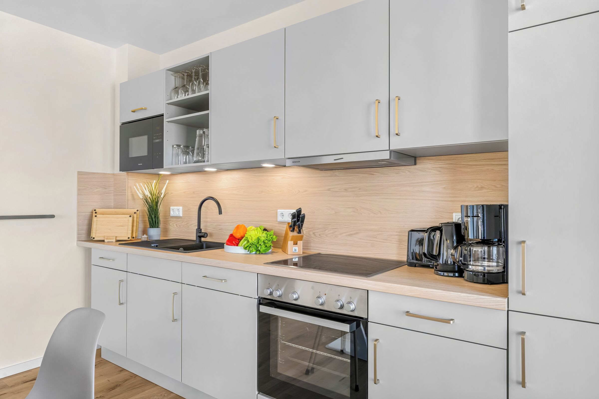 Una cocina moderna con gabinetes grises, horno empotrado, cafetera y un lavamanos.