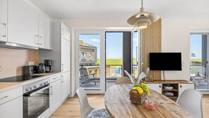 A modern kitchen with a dining area, a flat-screen TV, and a view of the outdoors. - The View B04 Briese - Garden furniture, elevator, shared Sauna, parking space (Dagebüll)
