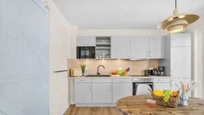 A modern kitchen with white cabinetry, a wooden countertop, and a round dining table with a fruit basket. - The View B04 Briese - Garden furniture, elevator, shared Sauna, parking space (Dagebüll)