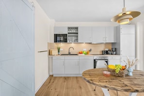 A modern kitchen with white cabinetry, a wooden countertop, and a round dining table with a fruit basket. - The View B04 Briese - Garden furniture, elevator, shared Sauna, parking space (Dagebüll)