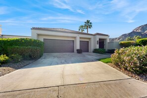 A residential house with two garage doors, a driveway, and surrounding greenery. - Glamorous home w/ mountain views, private pool, & on-site golf - 3 BR - #067092 (La Quinta)