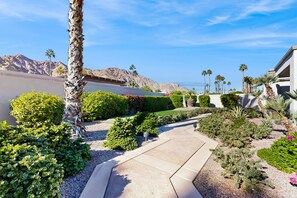 A landscaped garden with a pathway leading to a building, surrounded by various shrubs and palm trees. - Glamorous home w/ mountain views, private pool, & on-site golf - 3 BR - #067092 (La Quinta)