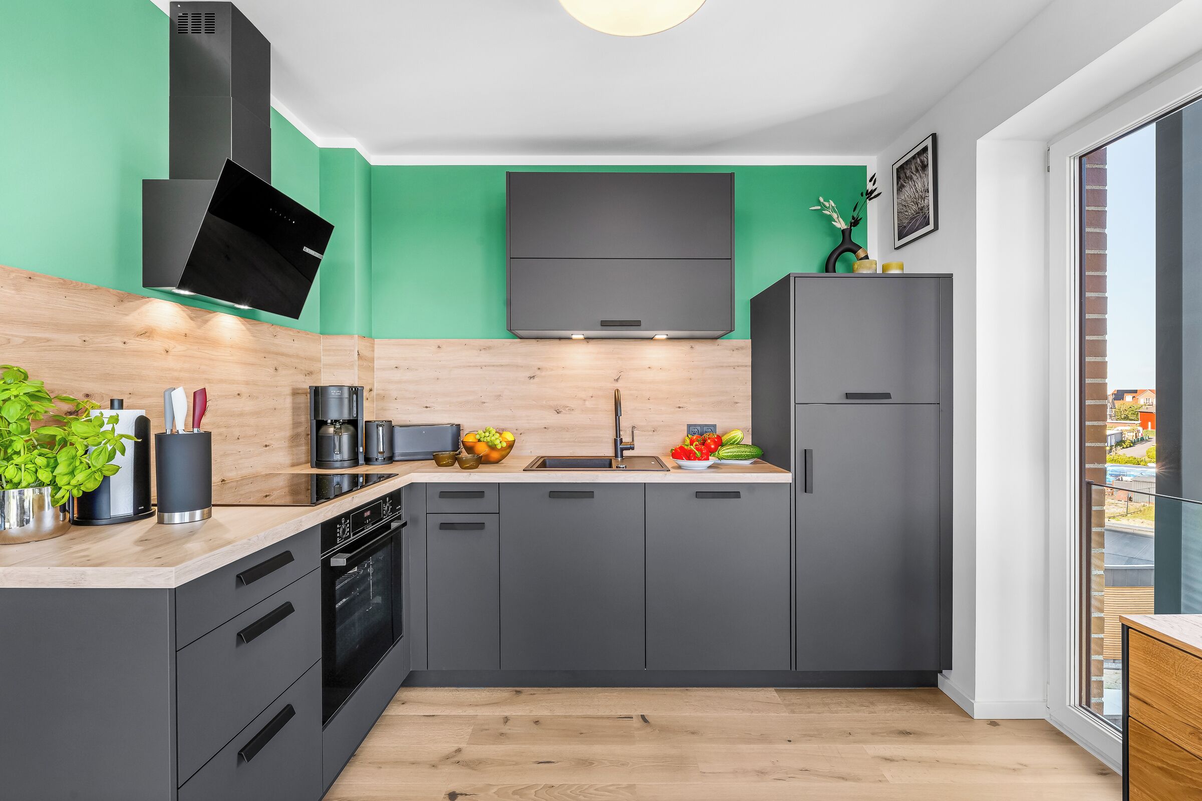 A modern kitchen with grey cabinets, a black range hood, and a green accent wall.