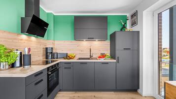 A modern kitchen with grey cabinets, a black range hood, and a green accent wall.