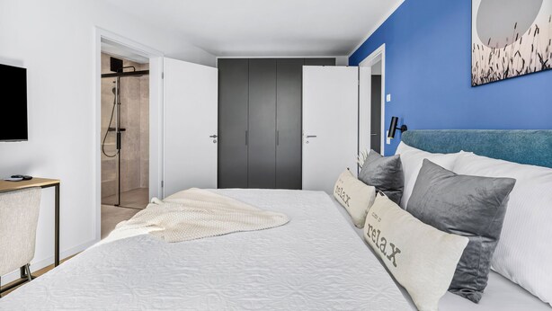 A bedroom with a bed, pillows, a TV, a desk, and a shower area. - The View B12 Zuhause bei Emi -Sea view,elevator, balcony, armchair, shared Sauna (Dagebüll)