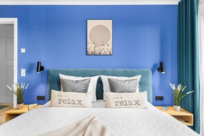 A bedroom with a blue wall, a bed with two pillows, a bedside table with a lamp, and a wall-mounted artwork. - The View B12 Zuhause bei Emi -Sea view,elevator, balcony, armchair, shared Sauna (Dagebüll)