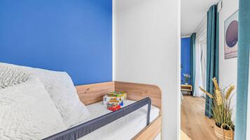 A room with a bed, a small table, a plant, and a wall with a painting.