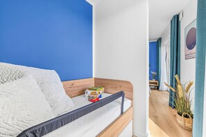 Una habitación con cama, una mesita, una planta y un cuadro en la pared.
