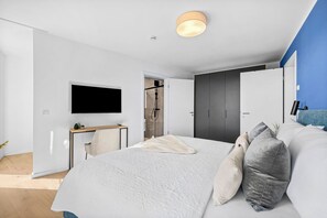 Een moderne slaapkamer met een groot bed, een aan de muur bevestigde televisie, een bureau met een stoel en een inloopkast.