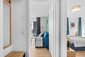 A modern hotel room with a wooden floor, a blue sofa, a bed with a white headboard, and a green accent wall. - The View B12 Zuhause bei Emi -Sea view,elevator, balcony, armchair, shared Sauna (Dagebüll)