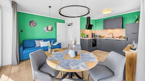 A modern living space with a blue sofa, a round dining table with grey chairs, a kitchen with a black range hood, and a green accent wall. - The View B12 Zuhause bei Emi -Sea view,elevator, balcony, armchair, shared Sauna (Dagebüll)