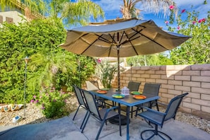 An outdoor patio with a table, chairs, and an umbrella. - Classic, dog-friendly home near golf with heated pool, enclosed yard & fireplace (Indio)