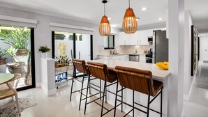 A modern kitchen with a central island, bar stools, pendant lighting, and a view of the outdoors. - Mtn-view home with private pool, large patio, streaming, fireplace, grill, & W/D (Palm Springs)