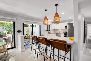 A modern kitchen with a central island, bar stools, pendant lighting, and a view of the outdoors. - Mtn-view home with private pool, large patio, streaming, fireplace, grill, & W/D (Palm Springs)