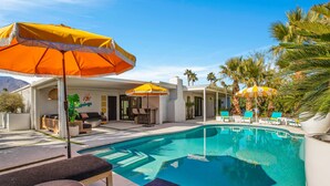 A pool area with lounge chairs and umbrellas, a patio with seating, and palm trees. - Mtn-view home with private pool, large patio, streaming, fireplace, grill, & W/D (Palm Springs)