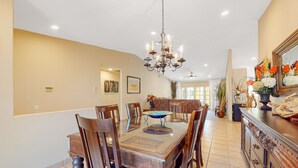 A dining area with a glass-top table, wooden chairs, a chandelier, and a decorative mirror. - Family-Friendly Home w/ an Outdoor Kitchen, Private Pool, & Spa - 3BR - #66708 (La Quinta)