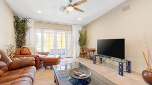 A living room with a leather sofa, a glass coffee table, a flat-screen TV, and a ceiling fan. - Family-Friendly Home w/ an Outdoor Kitchen, Private Pool, & Spa - 3BR - #66708 (La Quinta)